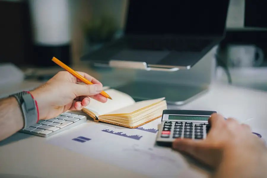 Image of a person reviewing financial documents with a calculator and notes, illustrating budgeting for a new business