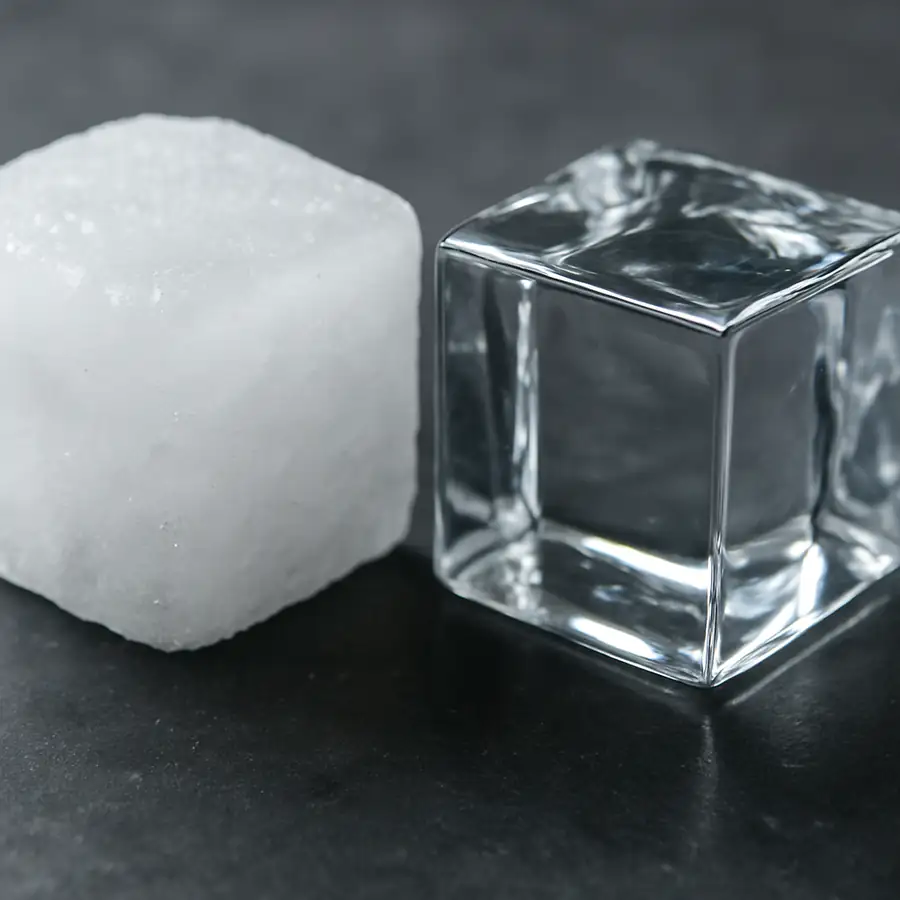 A close up comparison of a cloudy, white ice cube next to a perfectly clear gourmet ice cube