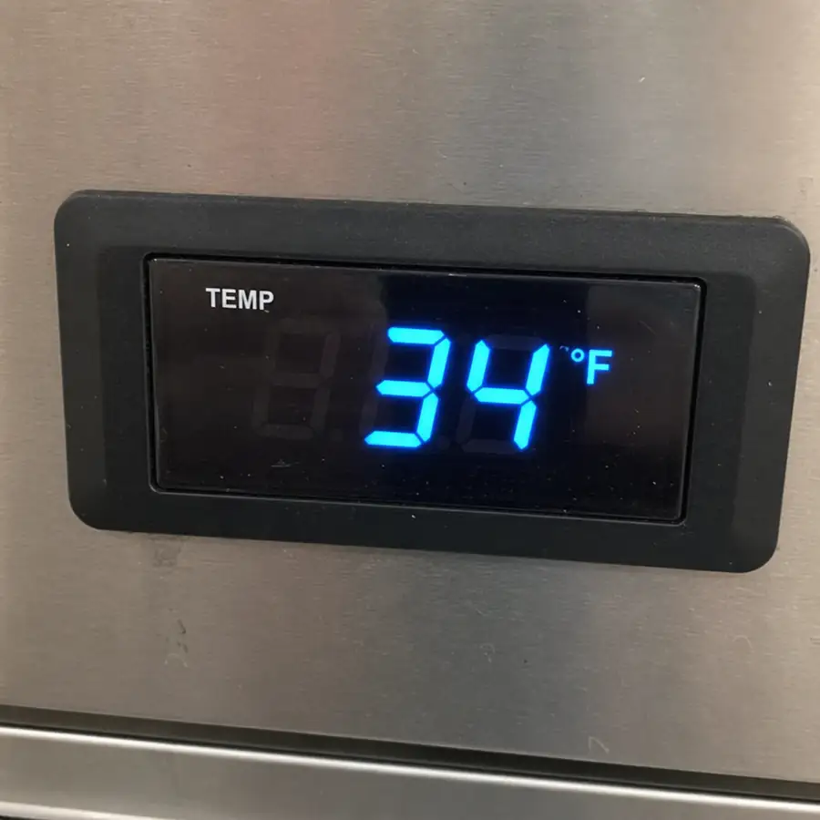 Close-up of a digital temperature gauge on a commercial refrigerator showing 34 degrees Fahrenheit in English