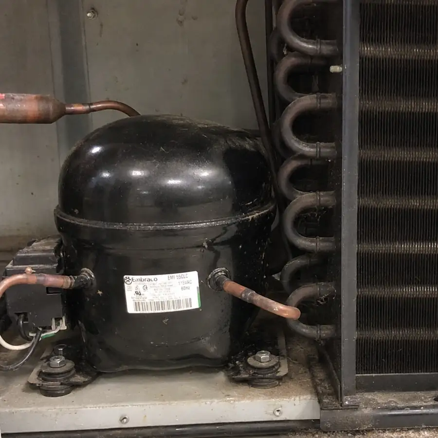 Close up of a commercial refrigerator compressor and condenser coils