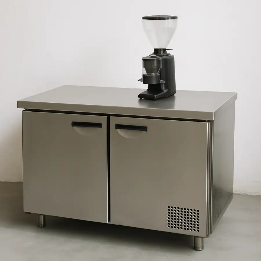 A stainless steel worktop refrigerator with a coffee grinder sitting on top.