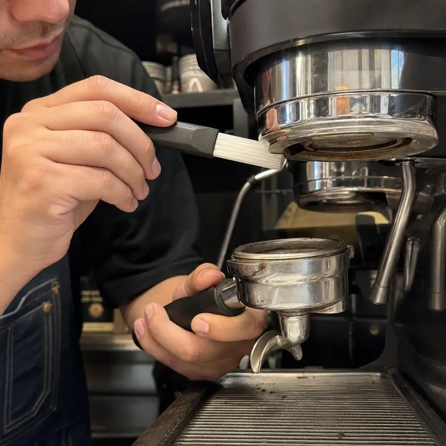 Close up of a barista carefully cleaning an espresso machine portafilter and group head with a specialized brush