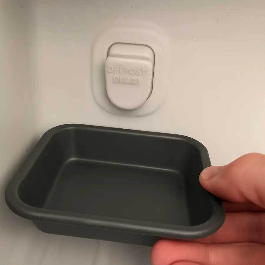 A close-up view of a standard defrost drain plug and how to position a tray beneath it to catch water.