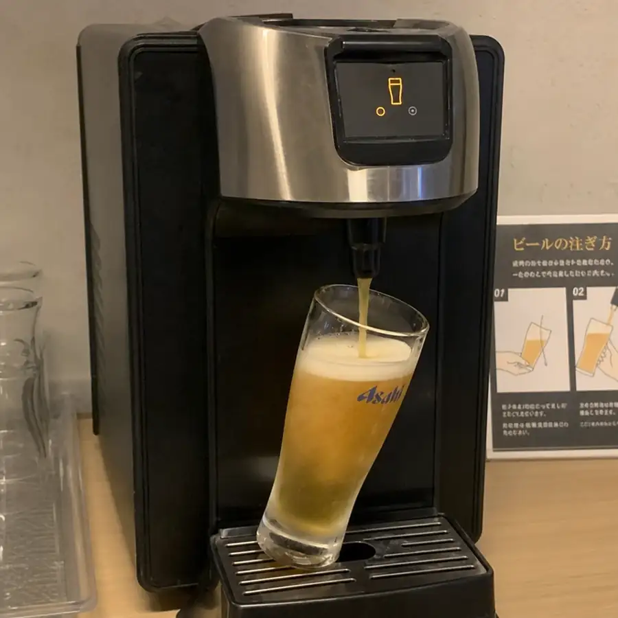 Automatic beer dispenser pouring beer into a tilted glass, with a pour-instruction card beside the machine