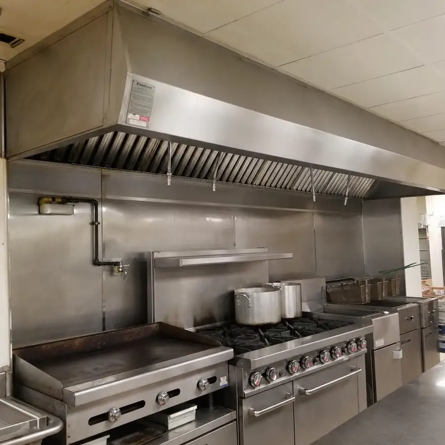 Stainless steel commercial exhaust hood with baffle filters and fire suppression nozzles over a griddle, gas range, and deep fryers