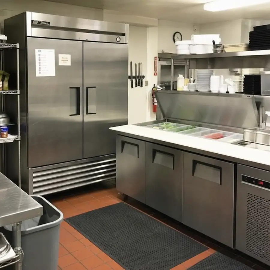 Stainless True two-door reach-in refrigerator beside an open refrigerated sandwich prep table with ingredient pans in a commercial kitchen