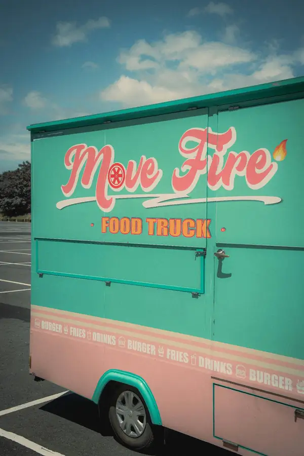 Teal and salmon Move Fire food truck in a sunny parking lot with retro branding and burger, fries, and drinks icons