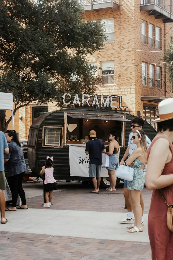 Vintage CARAMEL food trailer with a marquee sign and wooden serving hatch in a busy urban plaza with customers