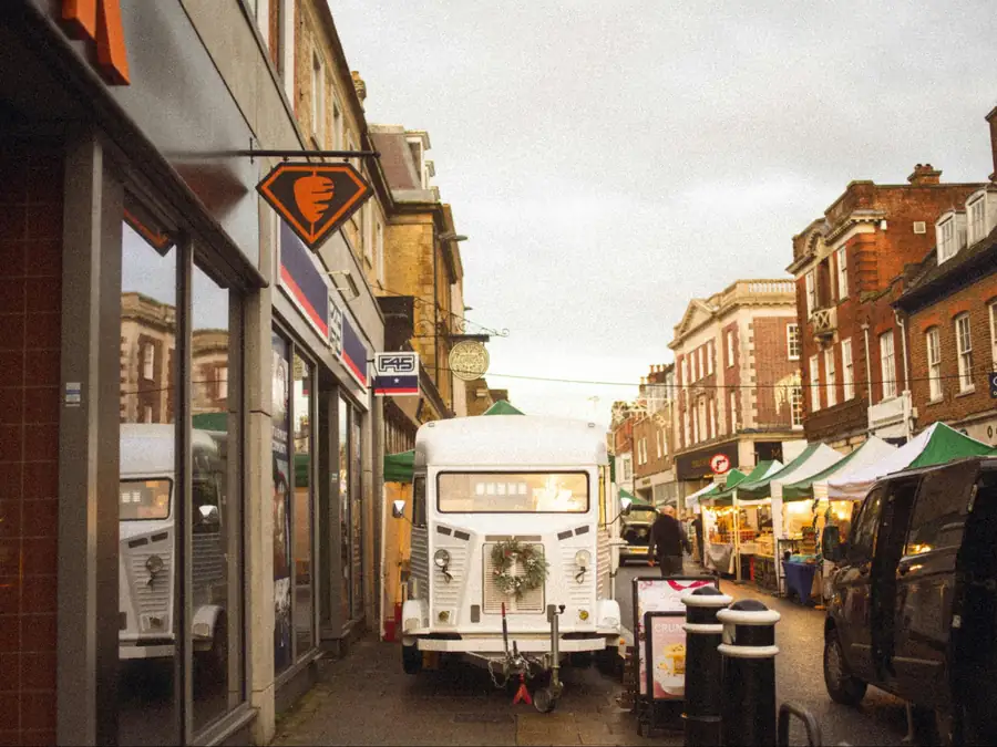 White vintage food truck trailer with a Christmas wreath parked on a historic street market beside striped stall canopies