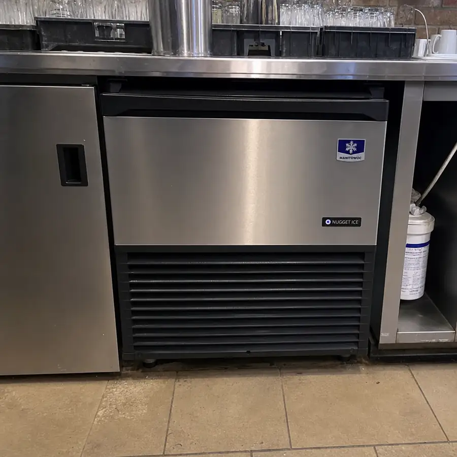 Undercounter nugget ice machine built into a bar, with glass racks above and a water filter beside the cabinet