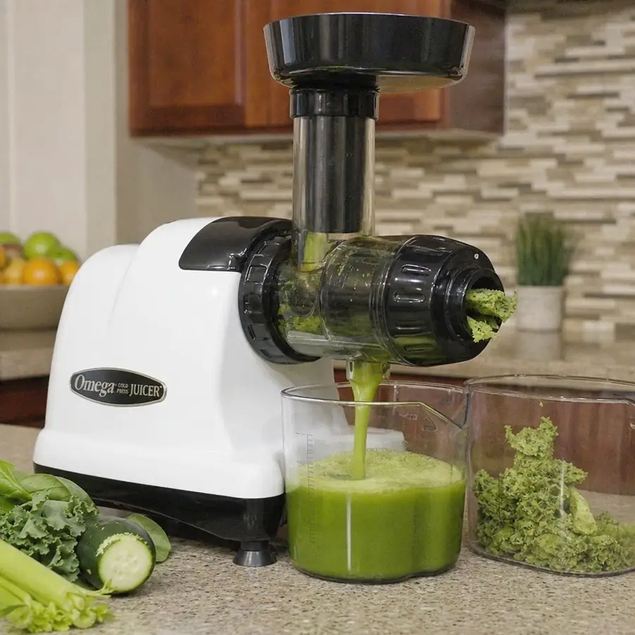 White Omega horizontal cold press juicer extracting green juice from kale, cucumber, and celery into a pitcher