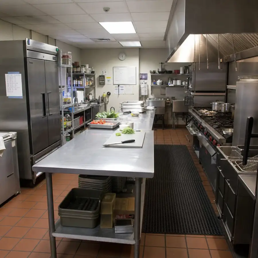 Professional commercial kitchen with stainless steel prep tables, a large refrigerator, gas range, and exhaust hood