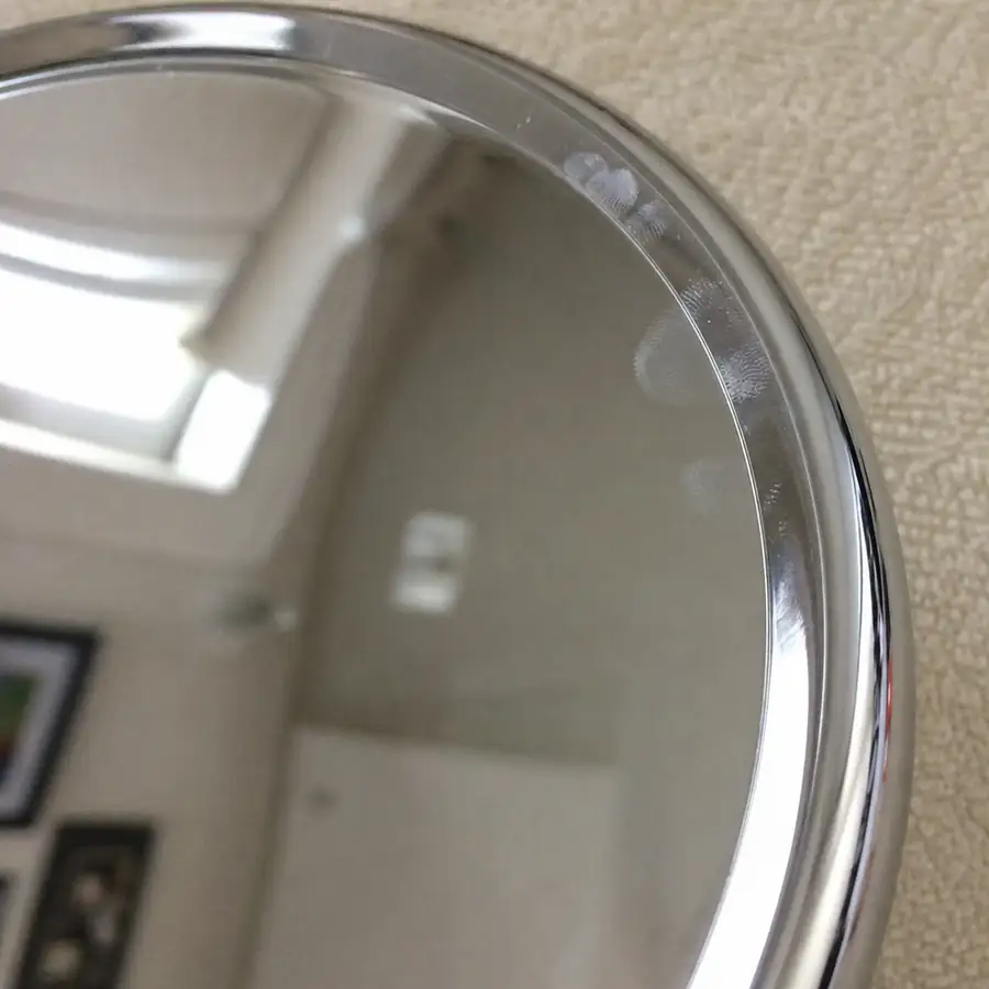 Close-up of a round stainless steel serving tray with mirror finish showing fingerprints on the polished rim