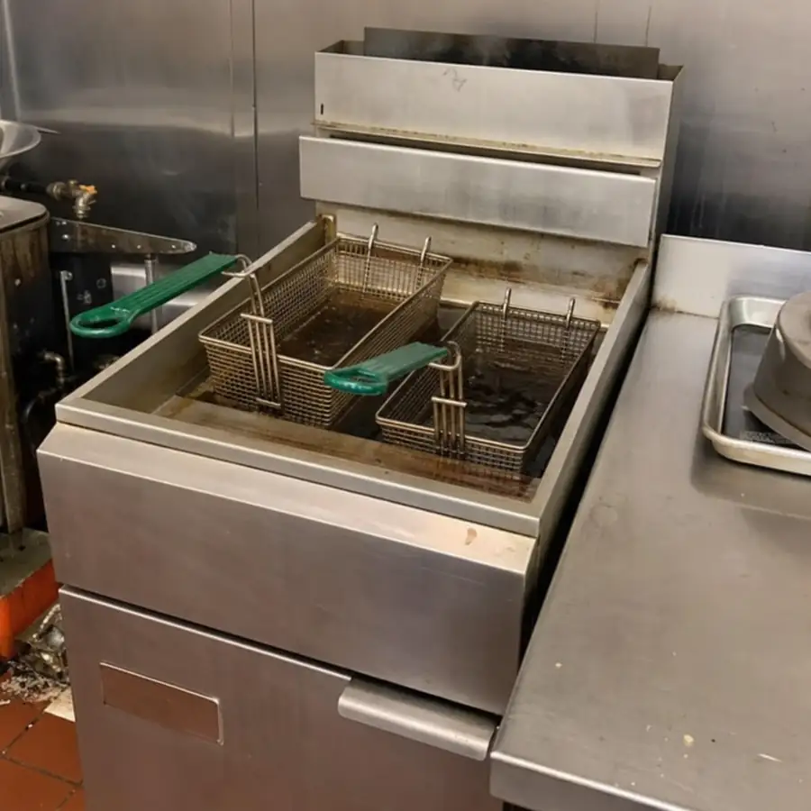 Worn floor-model commercial fryer with two baskets and green handles sitting in oil