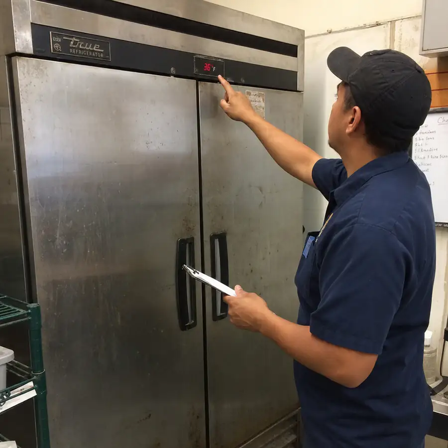 Technician in a navy shirt and cap checks a 36 degree display on a two-door commercial refrigerator
