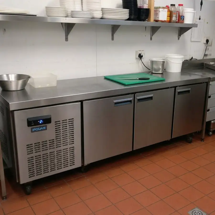 Stainless steel commercial worktop refrigerator used as a prep station in a restaurant kitchen