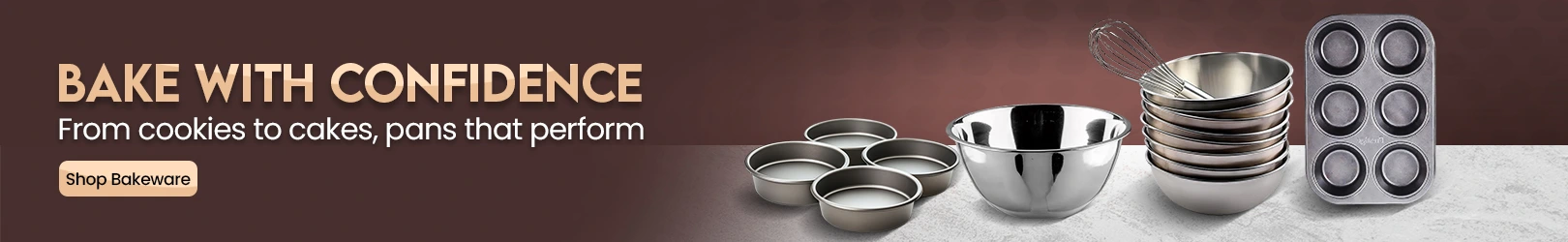 Assorted stainless steel mixing bowls, baking pans, and a muffin tray displayed on a light stone countertop with a maroon patterned background.